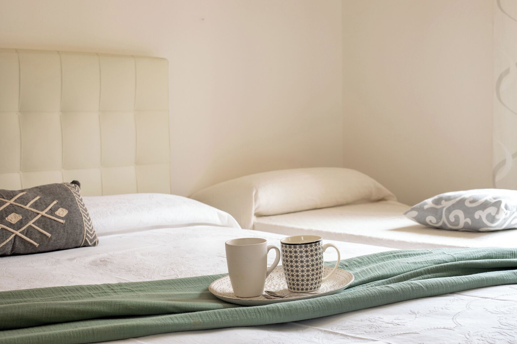 A neatly made bed with pillows, a cup, and a saucer on a white surface.