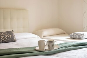 A neatly made bed with pillows, a cup, and a saucer on a white surface. - Sun and Sea - Alghero (Alghero)