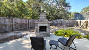 A backyard with a stone fire pit, two wicker chairs, and a wooden fence. - " Tiny Getaway " 2 Bedrooms 1 Bath Home (Supply)