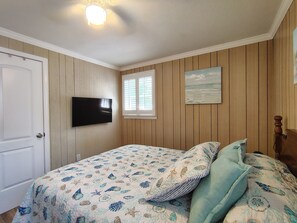 A bedroom with a bed, a television mounted on the wall, a window with blinds, and a painting on the wall. - " Tiny Getaway " 2 Bedrooms 1 Bath Home (Supply)