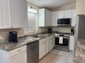 A kitchen with white cabinets, a stainless steel refrigerator, a microwave, an oven, a dishwasher, and a coffee maker. - Cozy 2-bedroom house in peaceful Hernando Beach with Dock (Hernando Beach)