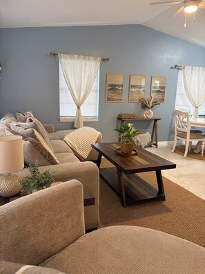 A living room with a sofa, a coffee table, and a dining area with a chair and table. - Cozy 2-bedroom house in peaceful Hernando Beach with Dock (Hernando Beach)