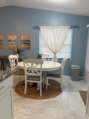 A dining area with a round table, white chairs, a woven rug, and a window with curtains. - Cozy 2-bedroom house in peaceful Hernando Beach with Dock (Hernando Beach)