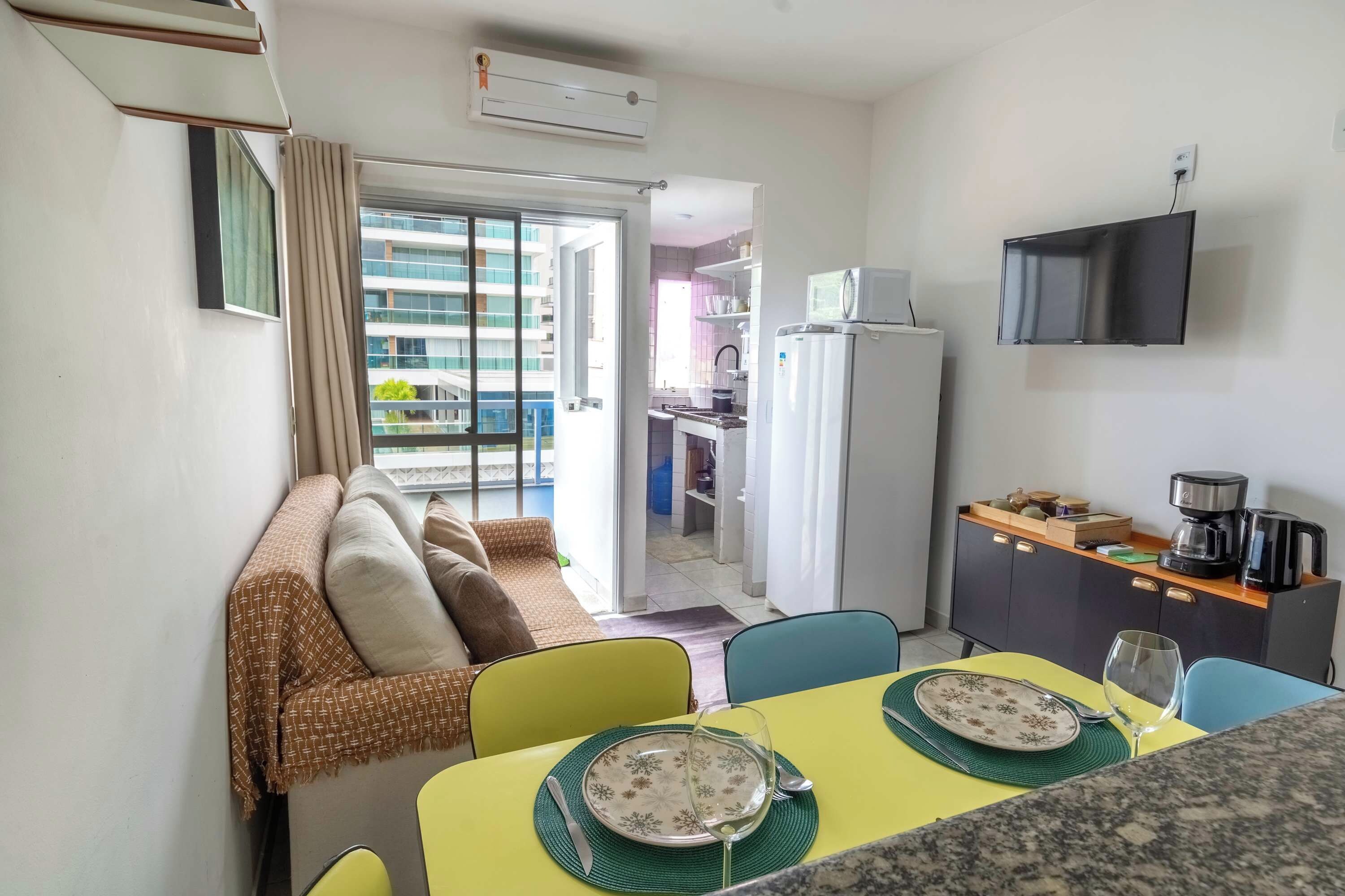 Un espace de vie compact comprenant un coin repas, une kitchenette et un balcon avec vue sur un immeuble.