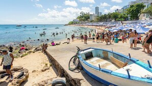 Uma praia com uma fileira de barcos, uma bicicleta e pessoas aproveitando a água.