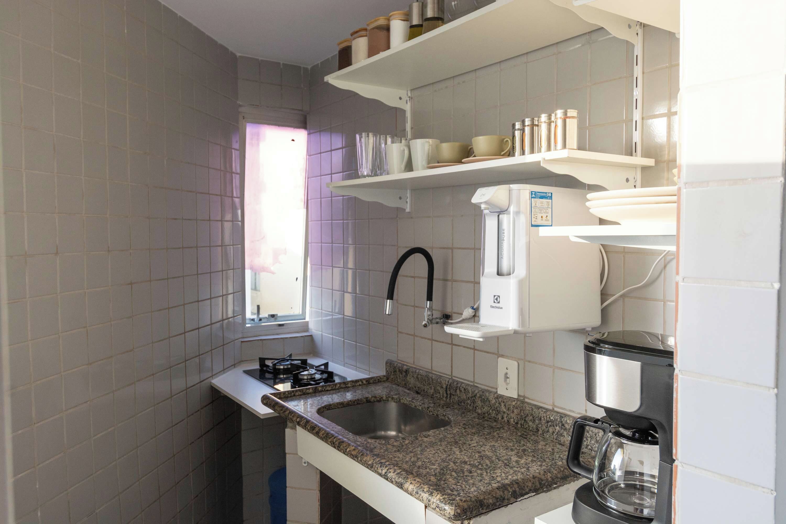 Una cocina con estufa a gas, un lavamanos, una cafetera y dispensador de agua.