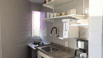 Una cocina con estufa a gas, un lavamanos, una cafetera y dispensador de agua.