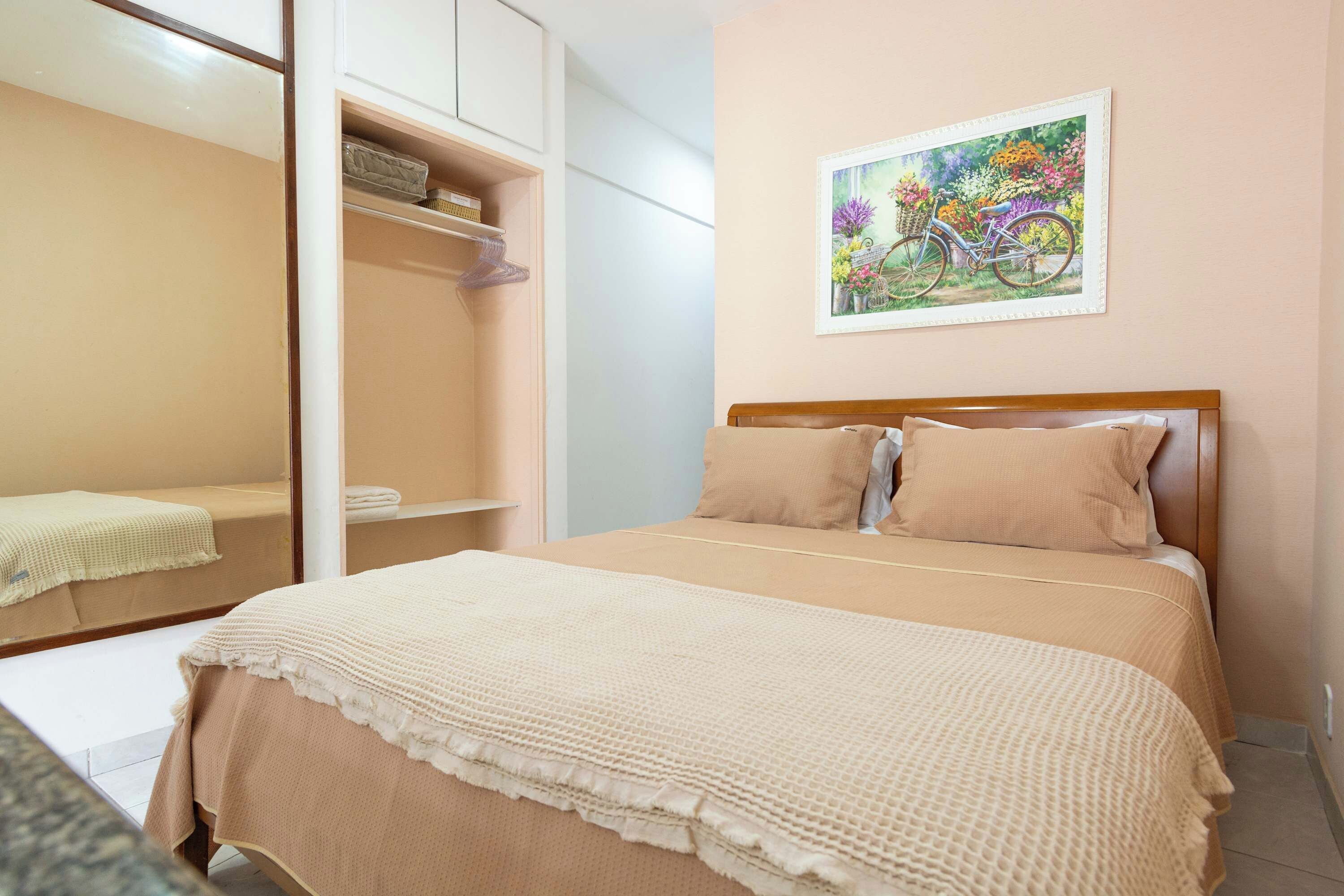 Un dormitorio con cama, armario, espejo y un cuadro en la pared.