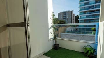 A balcony with artificial grass, a potted plant, and a view of a modern building.