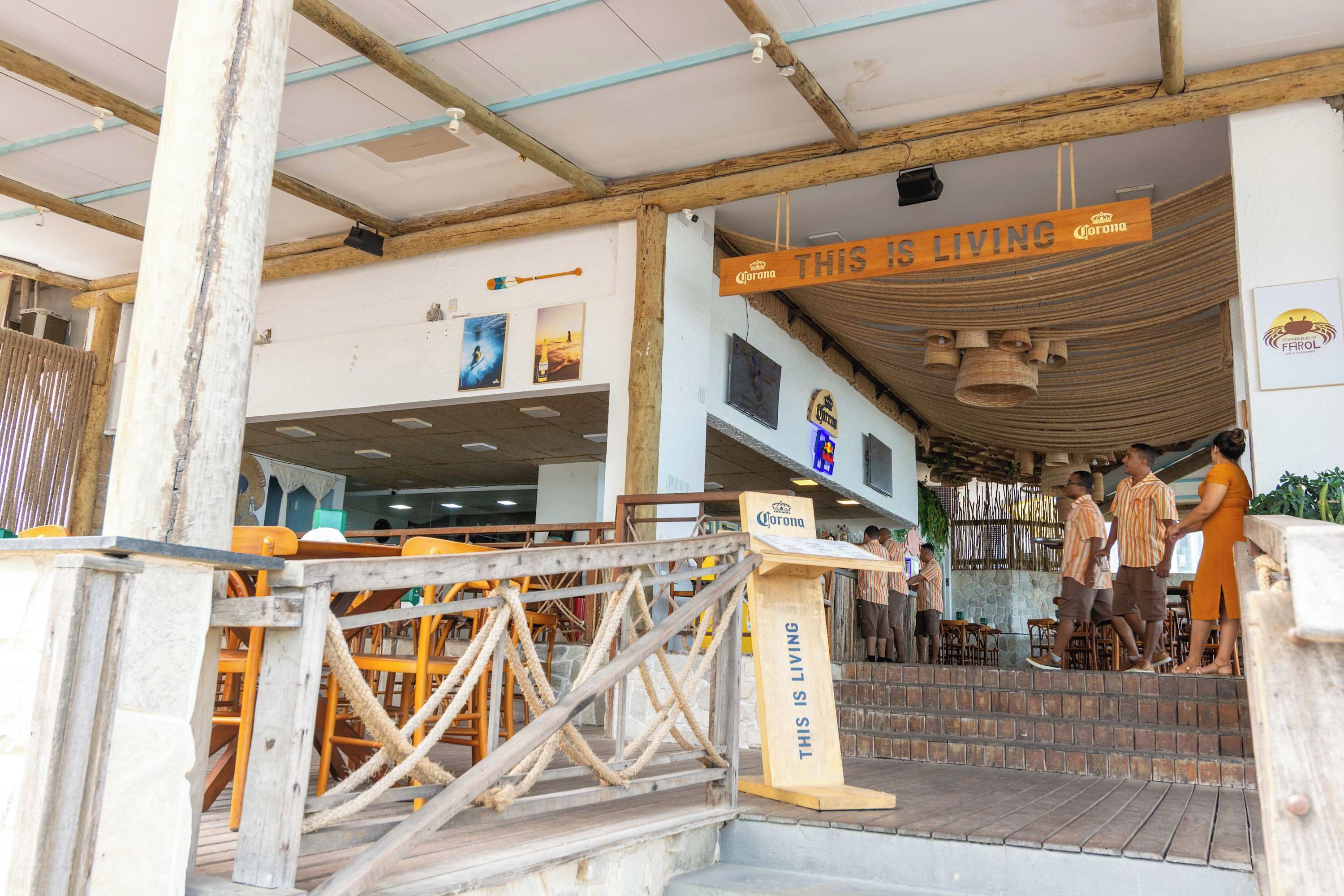 Un restaurante con entrada de madera, mesas al aire libre y un letrero que dice 'THIS IS LIVING'.