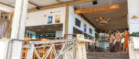 A restaurant with a wooden entrance, outdoor seating, and a sign that reads 'THIS IS LIVING'.