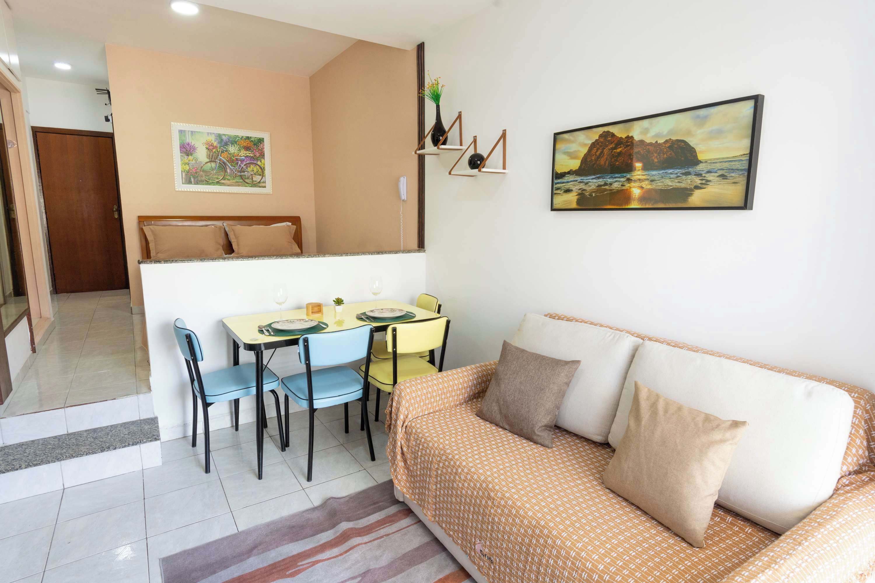 A compact living space with a dining area, a sofa, and a painting of a beach scene.