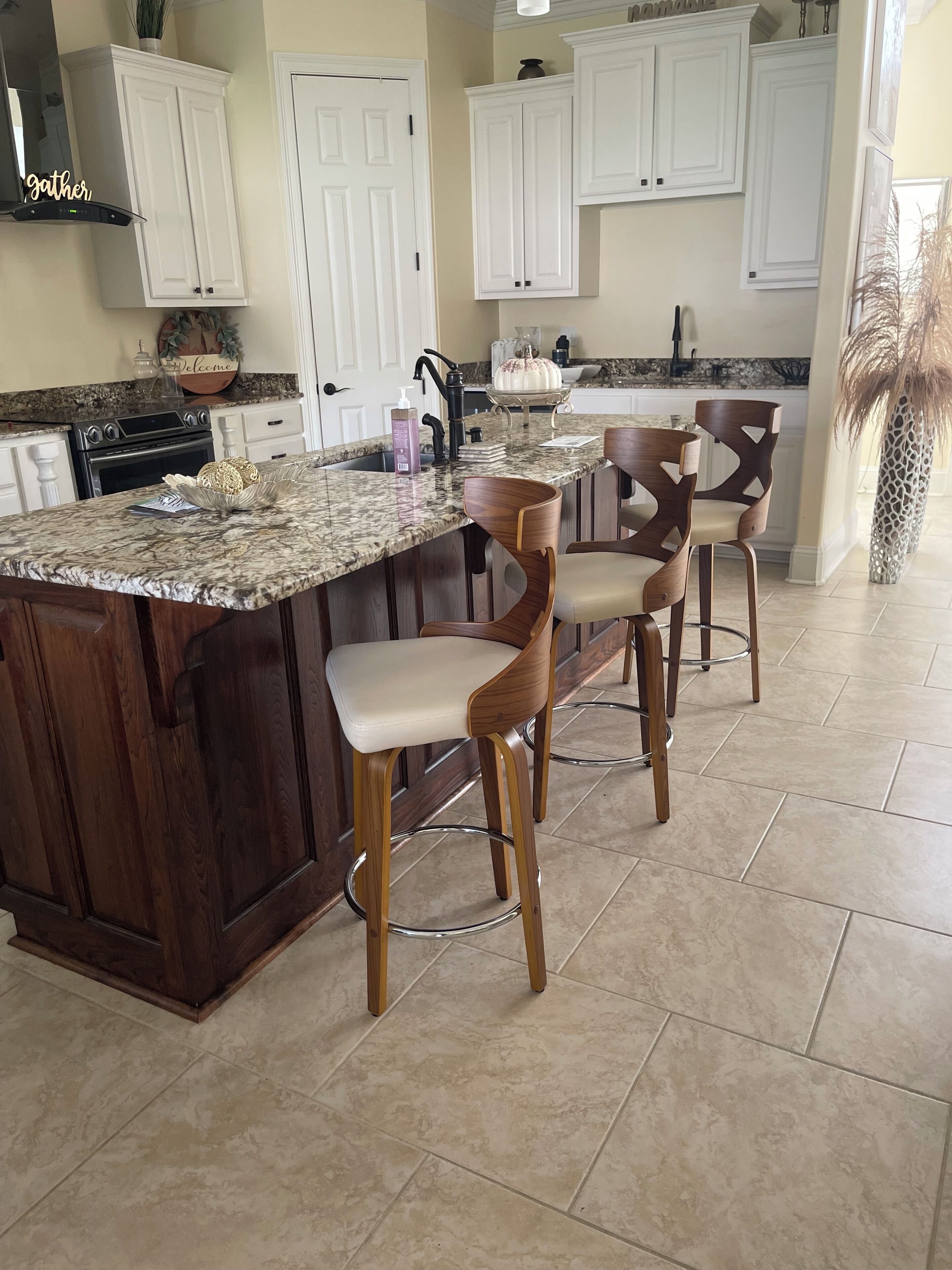 A kitchen with a central island, bar stools, white cabinets, and a tiled floor.
