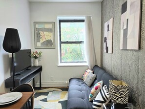 Un salon avec un canapé, un téléviseur à écran plat, une table basse et une fenêtre avec des rideaux.
