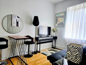 A modern living room with a television, a round mirror, a black desk, and a patterned cushion. - Chic One‑Bedroom Manhattan Apartment on Historic Strivers Row (New York)