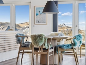 A dining area with a table and chairs, a pendant lamp, a framed picture, and a view of the landscape through large windows. - "Nuka" - 250m from the sea by Interhome (Hjørring)