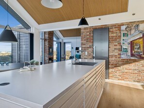 A modern kitchen with a large island, a brick wall, and a view of the outdoors. - "Nuka" - 250m from the sea by Interhome (Hjørring)