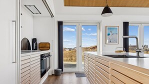 Een moderne keuken met een groot eiland, een inbouwoven en uitzicht door de glazen deur.
