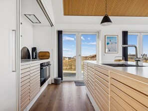 A modern kitchen with a large island, built-in oven, and a view through the glass door. - "Nuka" - 250m from the sea by Interhome (Hjørring)