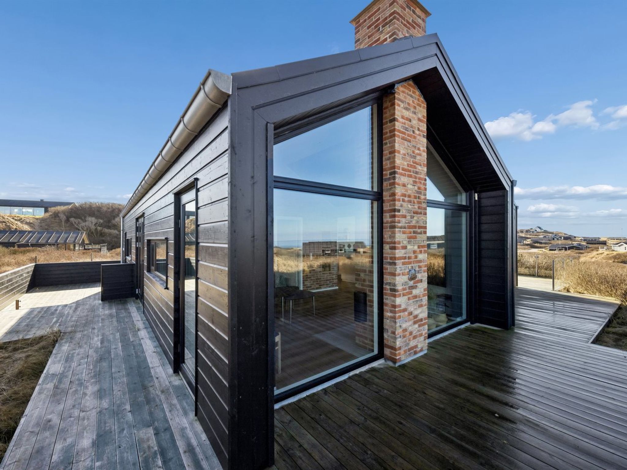 Ein modernes Haus mit großen Glasfenstern, einer Holzdiele und einem Backsteinsschornstein.