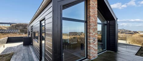 Een modern huis met grote glasramen, een houten terras en een bakstenen schoorsteen.