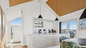 Een moderne keuken met witte kasten, een eetgedeelte met een ronde tafel en uitzicht op het landschap door grote ramen.