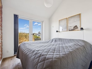 A bedroom with a large bed, a sliding glass door to a balcony, and two framed pictures on the wall. - "Nuka" - 250m from the sea by Interhome (Hjørring)