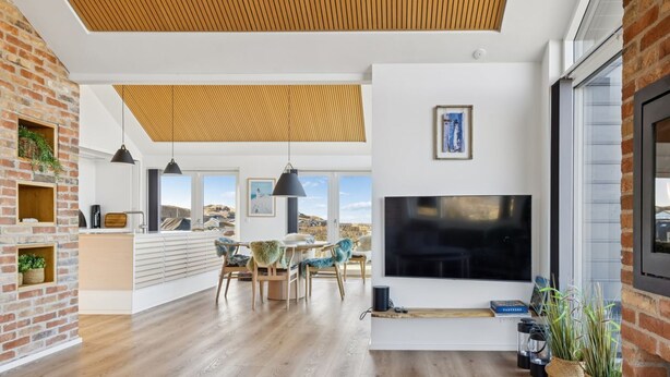 Een moderne woonkamer met een grote televisie, houten vloeren en uitzicht op het landschap.