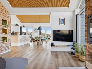 Een moderne woonkamer met een grote televisie, houten vloeren en uitzicht op het landschap.