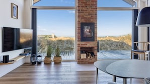 Een moderne woonkamer met een grote televisie, een open haard en uitzicht op een natuurlandschap.