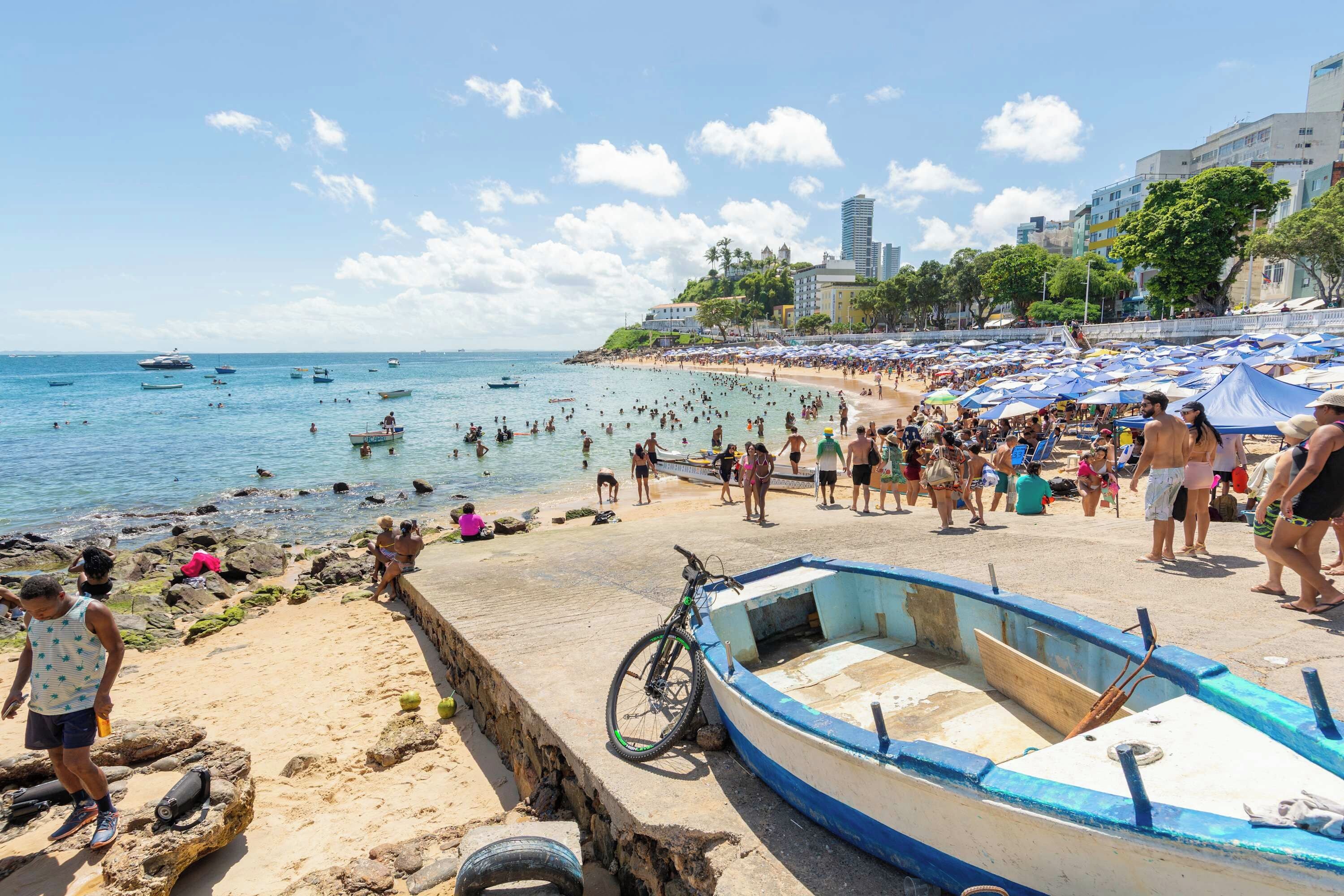 Una playa con una hilera de barcos, una bicicleta y gente disfrutando del agua.