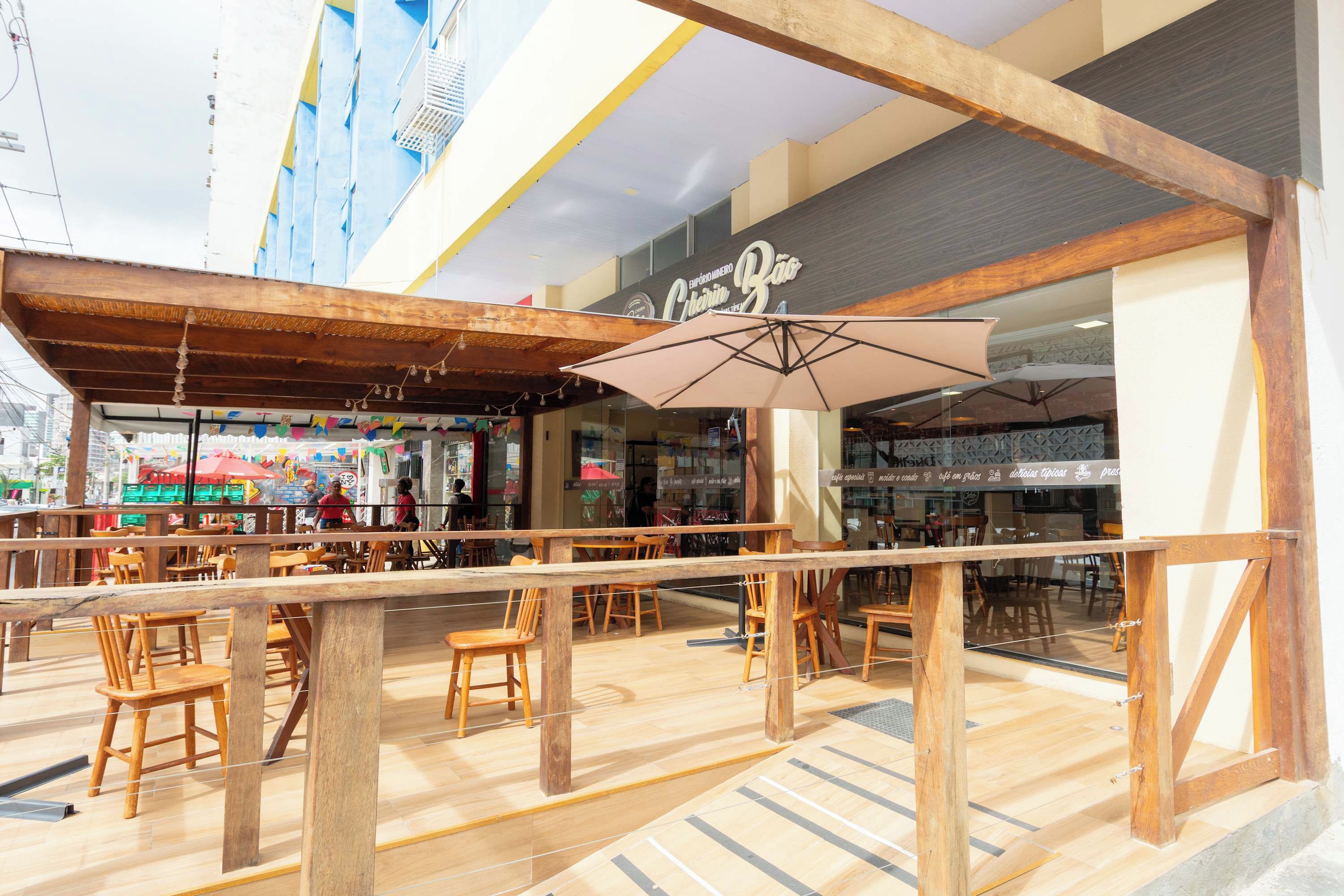 An indoor dining area with wooden tables and chairs, a large umbrella, and a view of a street with shops.