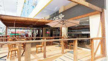 An indoor dining area with wooden tables and chairs, a large umbrella, and a view of a street with shops.
