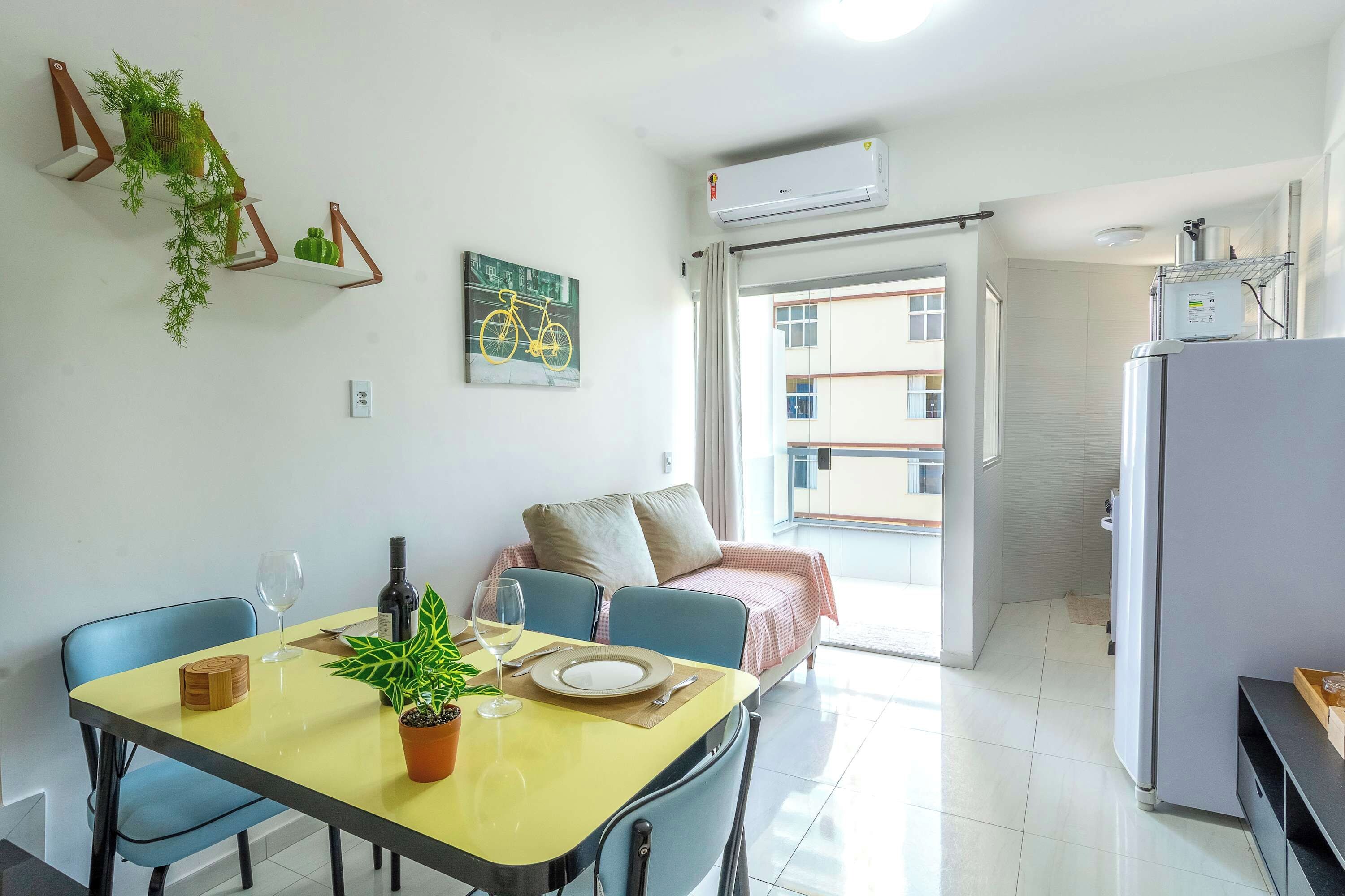 Un coin repas avec une table dressée pour deux personnes, une plante en pot et une œuvre d’art sur le thème du vélo accrochée au mur.