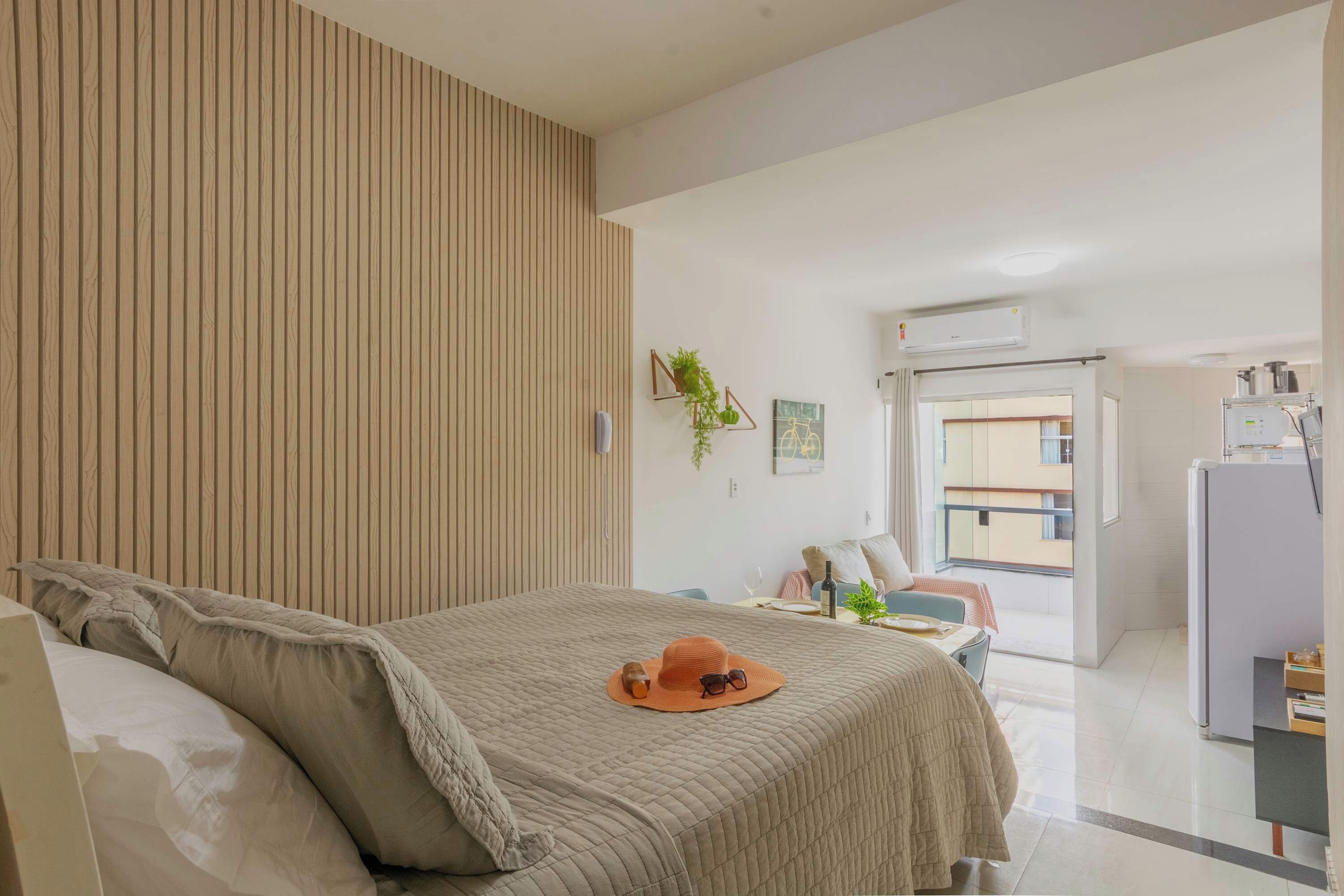 A hotel room with a bed, a desk, a chair, a plant, and an air conditioning unit.