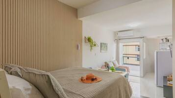 A hotel room with a bed, a desk, a chair, a plant, and an air conditioning unit.