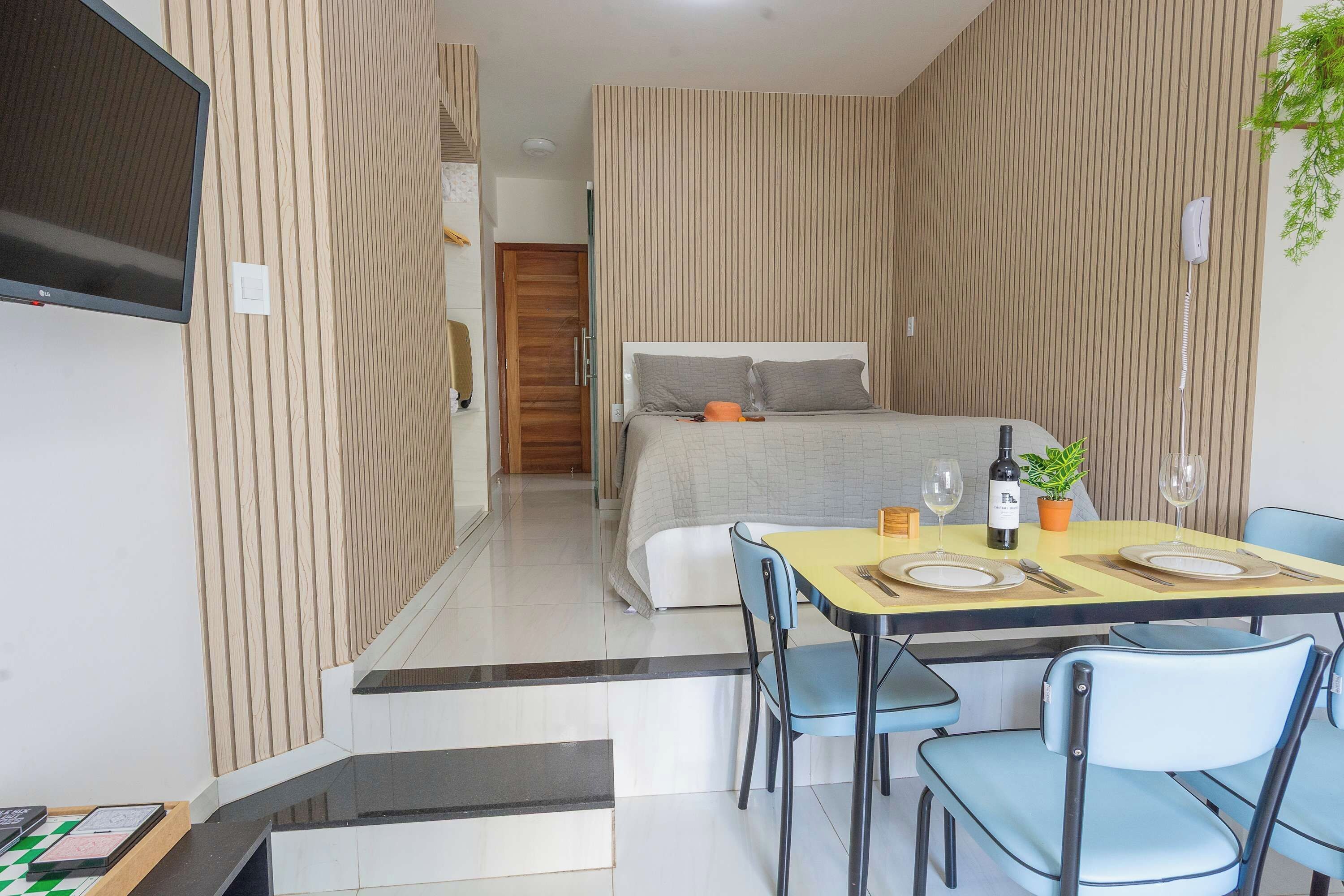 Una habitación de hotel moderna con una cama, un rincón de comedor con una mesa para dos personas y un televisor montado en la pared.