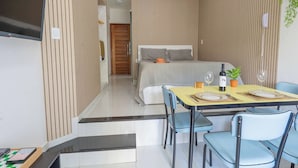 Quarto de hotel moderno com uma cama, área de refeições com mesa posta para dois e televisão fixada na parede.