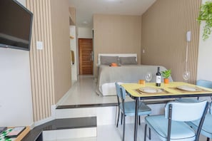 Una habitación de hotel moderna con una cama, un rincón de comedor con una mesa para dos personas y un televisor montado en la pared.