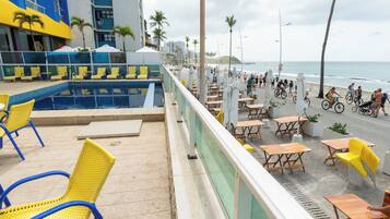 Área da piscina com cadeiras amarelas e azuis, piscina e vista para a praia e o oceano.