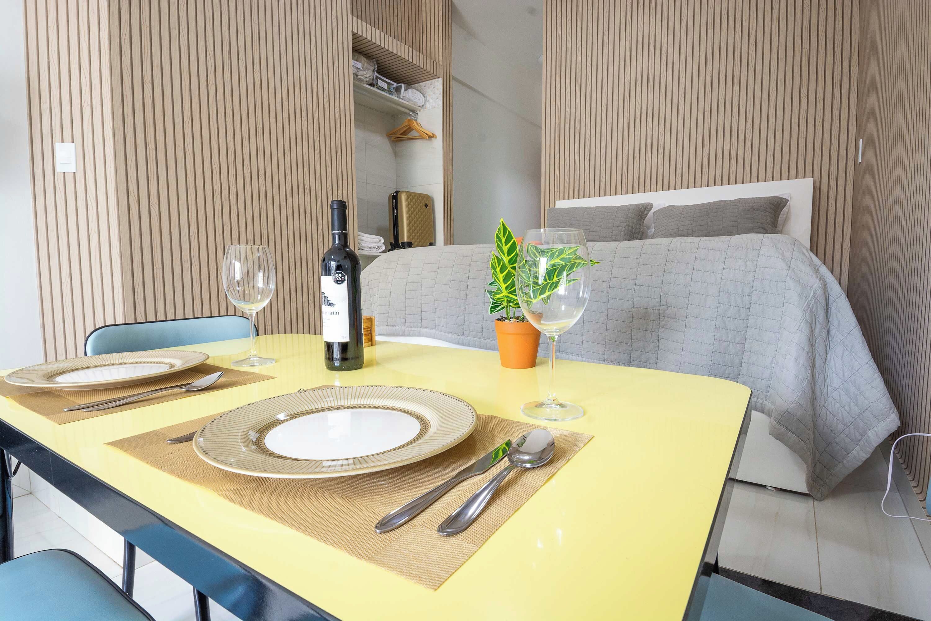 Une table à manger soigneusement dressée, avec des assiettes, des couverts et des verres à vin, le tout posé sur une nappe jaune.