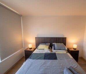 Un dormitorio con cama, dos mesitas de noche y una ventana.