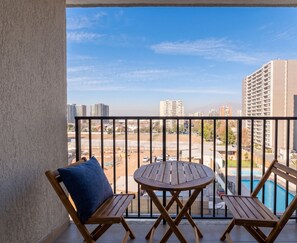 A balcony with a wooden table and two chairs, overlooking a swimming pool and a cityscape. - Guillemo Mann Ñuñoa by Domus Travels (Ñuñoa)