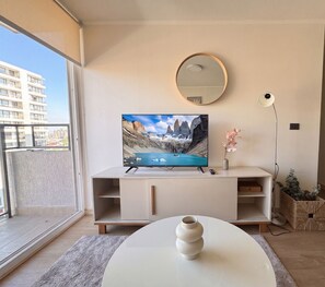 A modern living room with a television on a white stand, a round mirror on the wall, and a vase on a table. - Guillemo Mann Ñuñoa by Domus Travels (Ñuñoa)