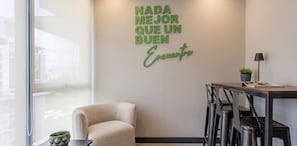Ein modernes Interieur mit einem an der Wand befestigten Schild mit der Aufschrift 'Nada mejor que un buen encuentro' und einem Essbereich mit Tisch, Stühlen und einer Topfpflanze.