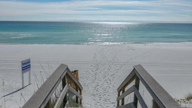 Una spiaggia con un cartello che indica accesso privato, una passerella di legno che conduce alla riva e impronte sulla sabbia.