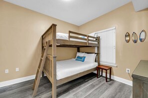 Una cama litera con escalera, una mesita de noche y una ventana con persianas.
