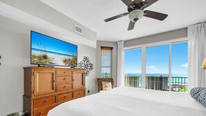 Una camera d'albergo con un letto grande, una ventola a soffitto, una TV su un mobile in legno e un balcone con vista sull'oceano.
