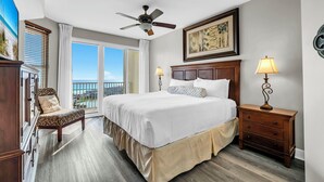 Una camera d'albergo con un letto, una sedia, un comodino, una ventola a soffitto e una finestra vista.