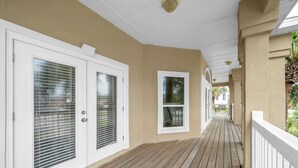 Une terrasse en bois couverte, dotée de rampes blanches et de murs de couleur beige.